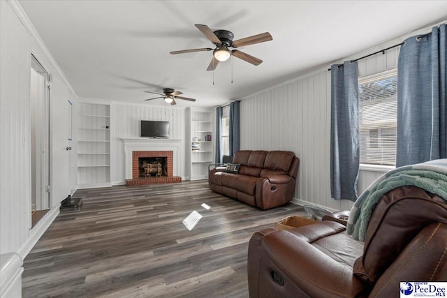 living area featuring ceiling fan, wood finished floors, built in features, a brick fireplace, and crown molding