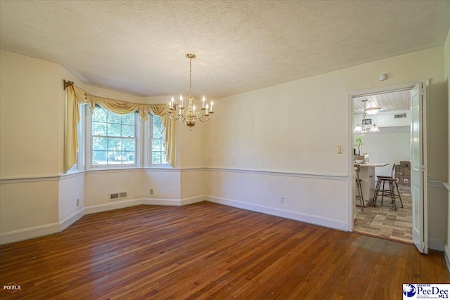 unfurnished room with hardwood / wood-style flooring, a textured ceiling, and a chandelier