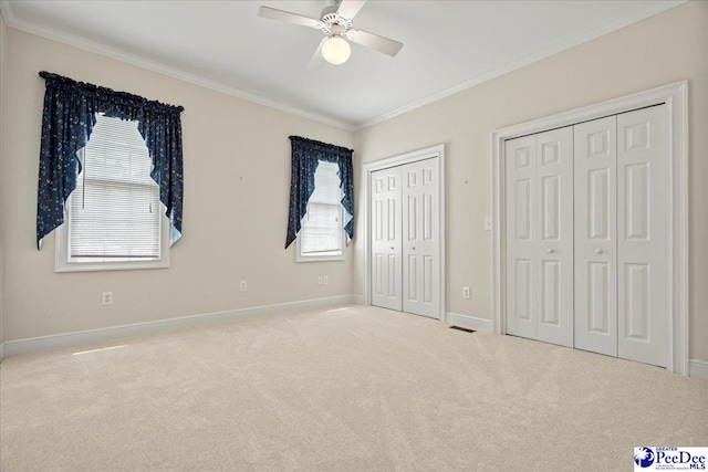 unfurnished bedroom featuring baseboards, visible vents, crown molding, multiple closets, and carpet floors