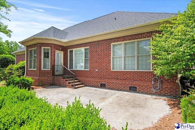 rear view of house with roof with shingles, a patio, brick siding, and crawl space