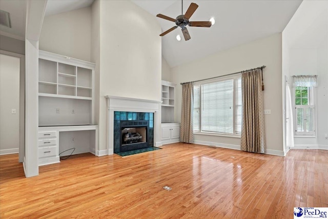 unfurnished living room featuring a ceiling fan, a tile fireplace, baseboards, high vaulted ceiling, and light wood-style floors