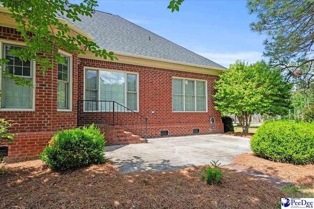 rear view of property featuring brick siding, crawl space, and roof with shingles