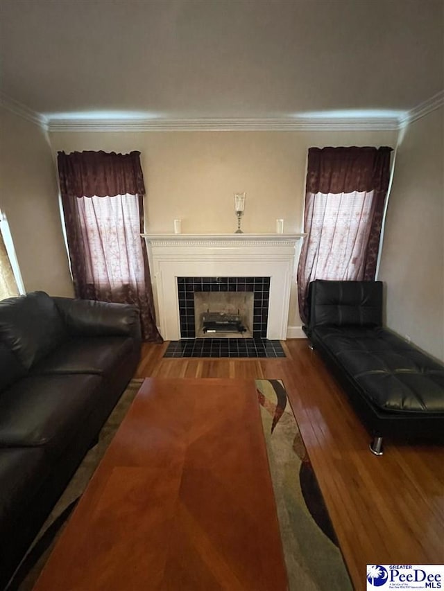 living room with crown molding, wood-type flooring, and a tiled fireplace