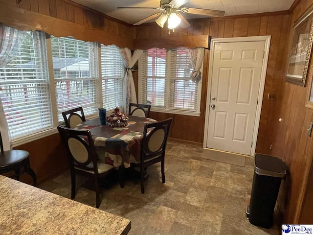 dining area with ornamental molding, ceiling fan, and wood walls