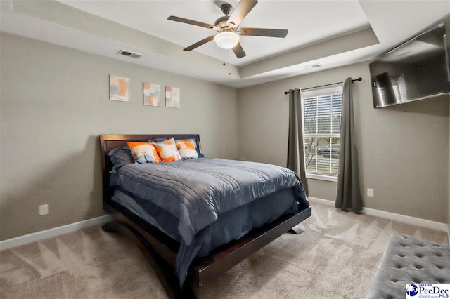 bedroom with ceiling fan, light colored carpet, and a tray ceiling