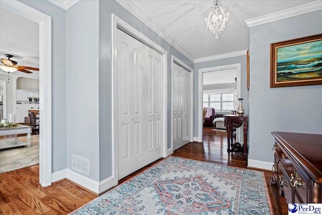 entryway with baseboards, wood finished floors, visible vents, and crown molding