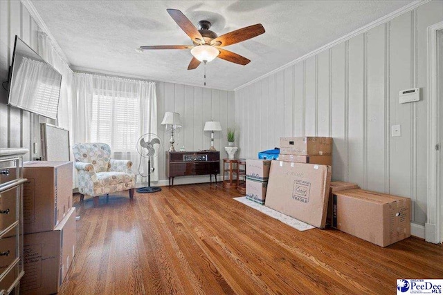 living area with a ceiling fan, a textured ceiling, ornamental molding, and wood finished floors