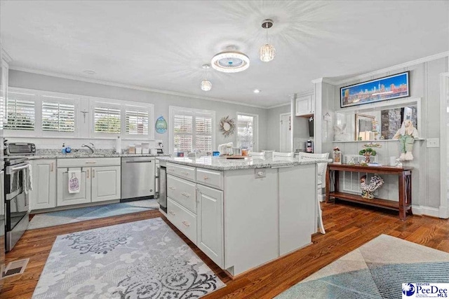 kitchen with visible vents, appliances with stainless steel finishes, light stone counters, wood finished floors, and crown molding