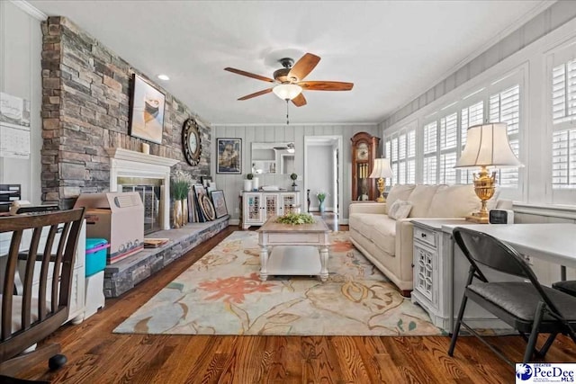 living room with ornamental molding, a stone fireplace, wood finished floors, and a ceiling fan