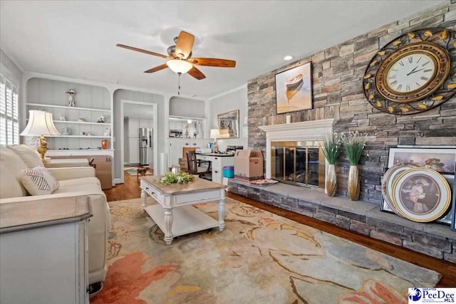 living area with ornamental molding, a fireplace, wood finished floors, and a ceiling fan