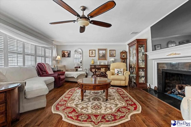 living area with visible vents, a ceiling fan, wood finished floors, crown molding, and a fireplace