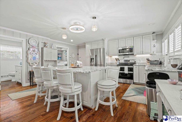 kitchen featuring dark wood finished floors, a kitchen island, appliances with stainless steel finishes, crown molding, and a kitchen bar