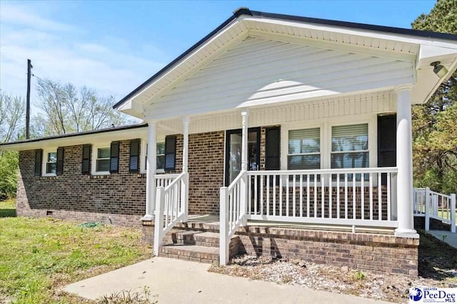 view of front of property featuring covered porch, crawl space, and brick siding