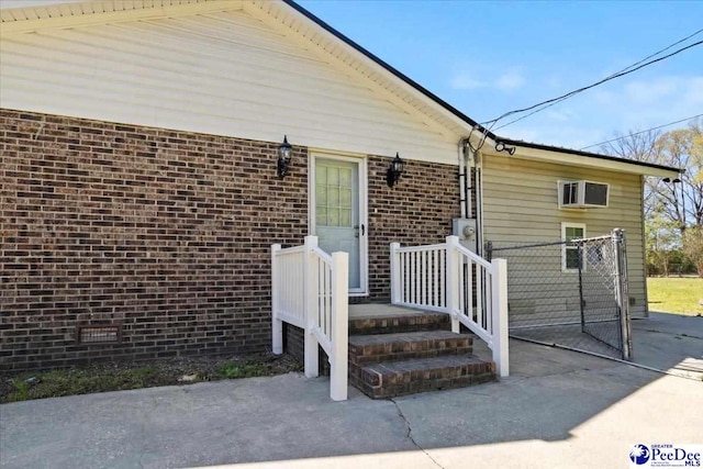 view of exterior entry with brick siding, crawl space, and an AC wall unit