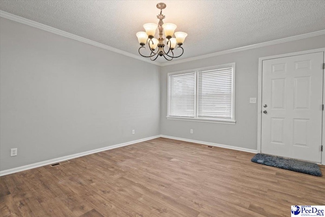 interior space with a textured ceiling, wood finished floors, ornamental molding, and an inviting chandelier