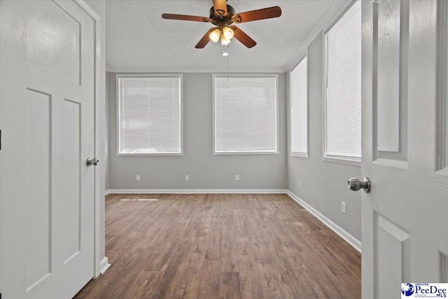 empty room with a ceiling fan, a textured ceiling, baseboards, and wood finished floors