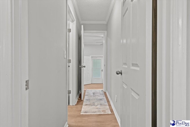 hallway with ornamental molding, baseboards, light wood finished floors, and a textured ceiling