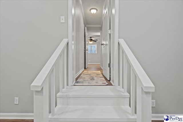 staircase featuring baseboards, ornamental molding, and a textured ceiling