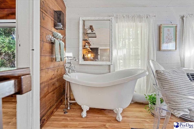 bathroom with a tub, hardwood / wood-style floors, and wooden walls