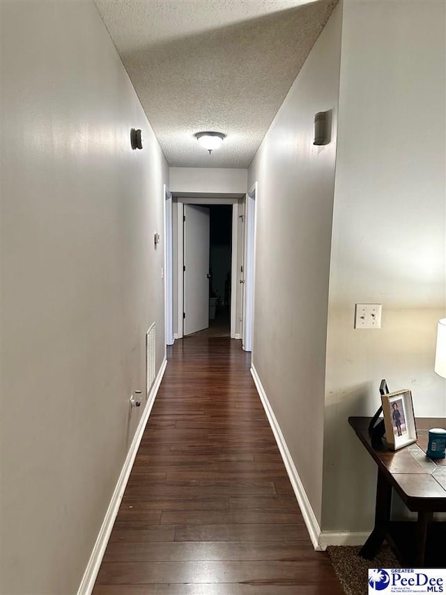 hallway featuring visible vents, hardwood / wood-style flooring, baseboards, and a textured ceiling