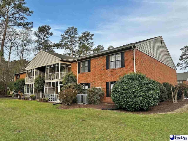 rear view of property featuring a lawn, cooling unit, a sunroom, and brick siding