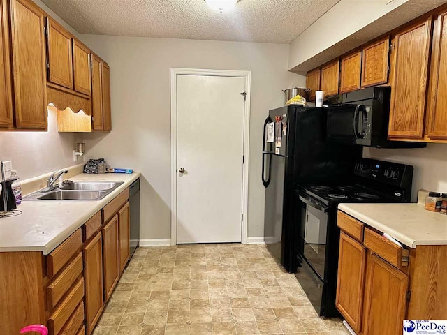 kitchen with a textured ceiling, light countertops, a sink, black appliances, and brown cabinetry
