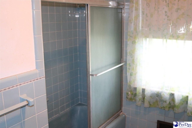 full bath featuring tile walls and bath / shower combo with glass door