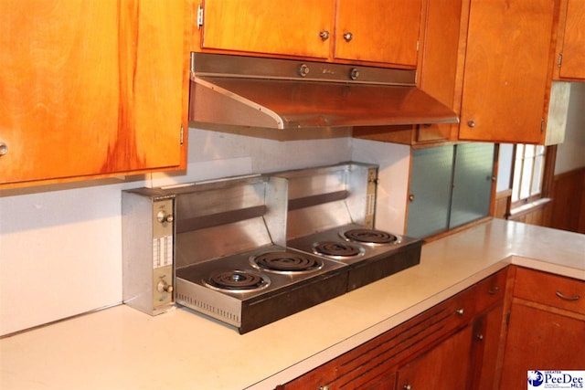 kitchen with under cabinet range hood, light countertops, and brown cabinetry