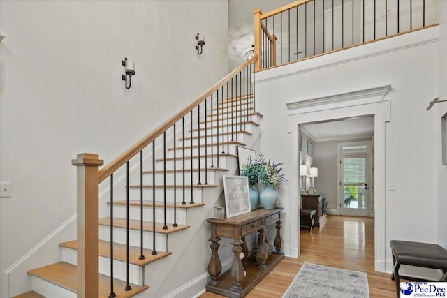 staircase featuring hardwood / wood-style floors, crown molding, and a high ceiling