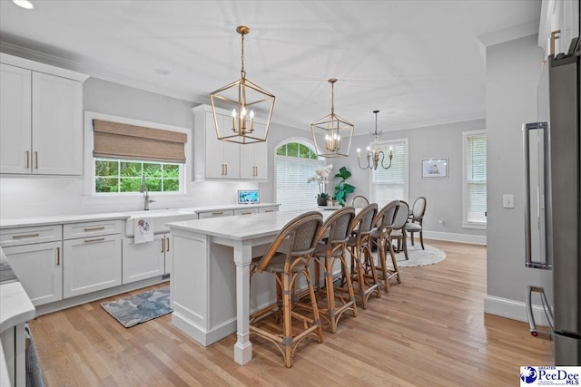 kitchen with white cabinets, a kitchen breakfast bar, hanging light fixtures, a center island, and crown molding