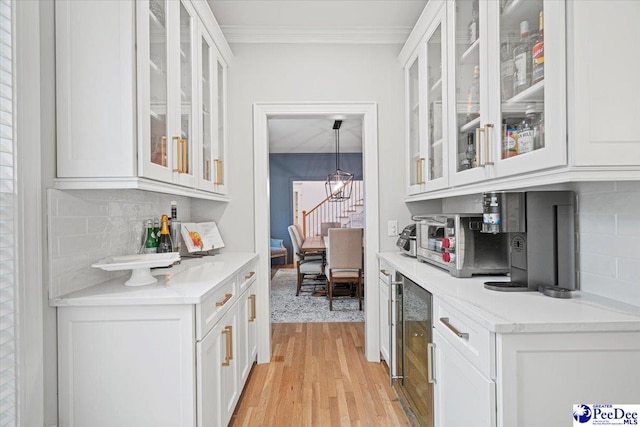 bar featuring crown molding, tasteful backsplash, decorative light fixtures, light hardwood / wood-style flooring, and white cabinets