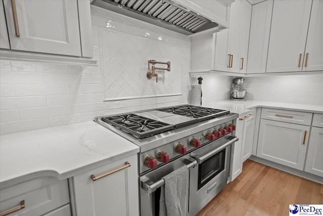 kitchen featuring tasteful backsplash, range with two ovens, custom exhaust hood, light stone counters, and light hardwood / wood-style flooring