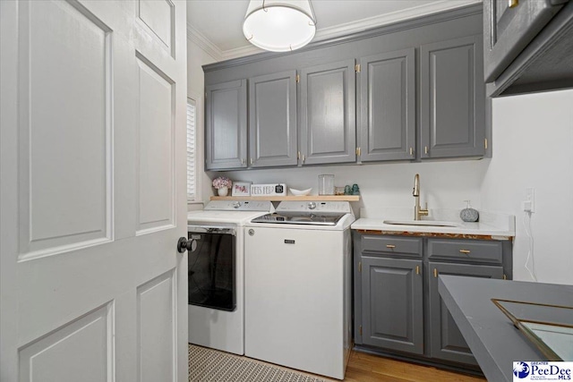 laundry area featuring sink, crown molding, cabinets, light hardwood / wood-style floors, and washer and dryer