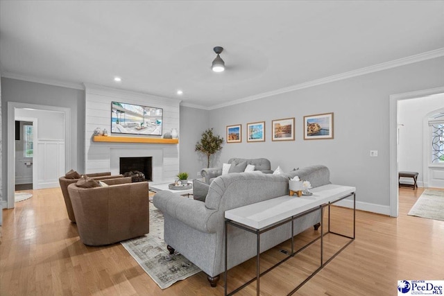 living room with a large fireplace, ornamental molding, and light hardwood / wood-style flooring