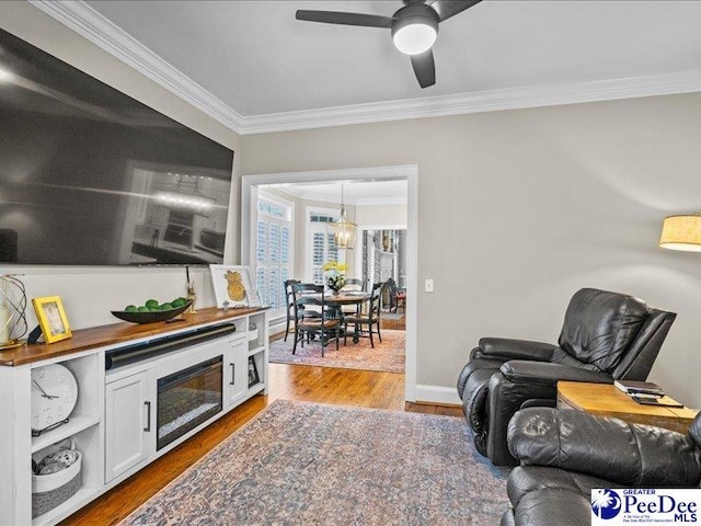 living area with ceiling fan with notable chandelier, baseboards, wood finished floors, and crown molding