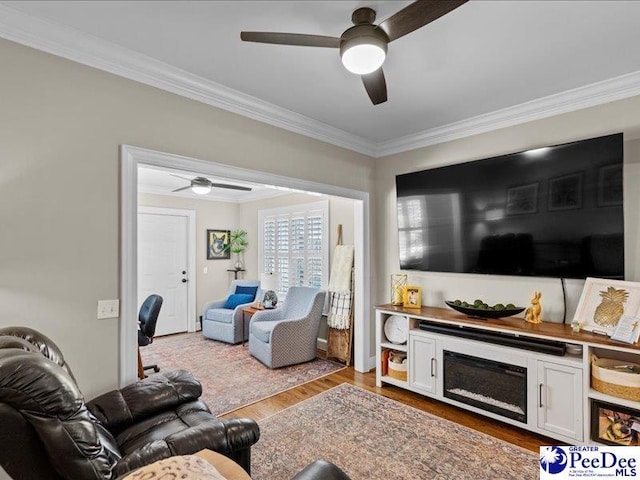 living area with ornamental molding, wood finished floors, and a ceiling fan