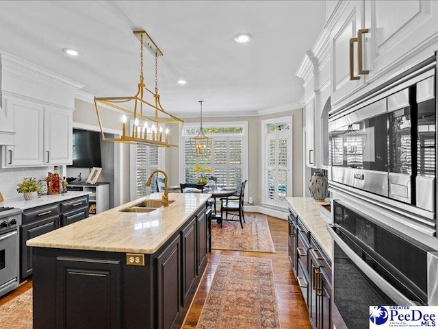 kitchen featuring appliances with stainless steel finishes, ornamental molding, wood finished floors, white cabinetry, and a sink