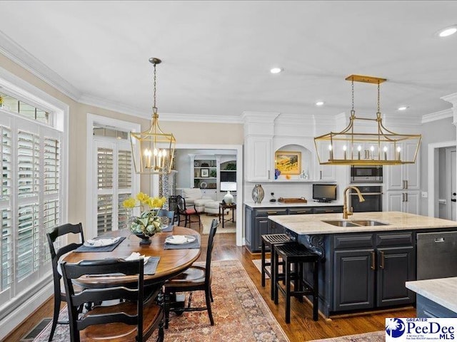 kitchen with a kitchen island with sink, a sink, ornamental molding, dark wood-style floors, and stainless steel microwave