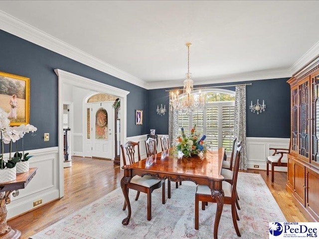 dining room with a chandelier, a wainscoted wall, ornamental molding, and light wood finished floors