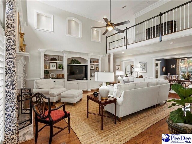 living area featuring crown molding, decorative columns, a towering ceiling, a ceiling fan, and wood finished floors