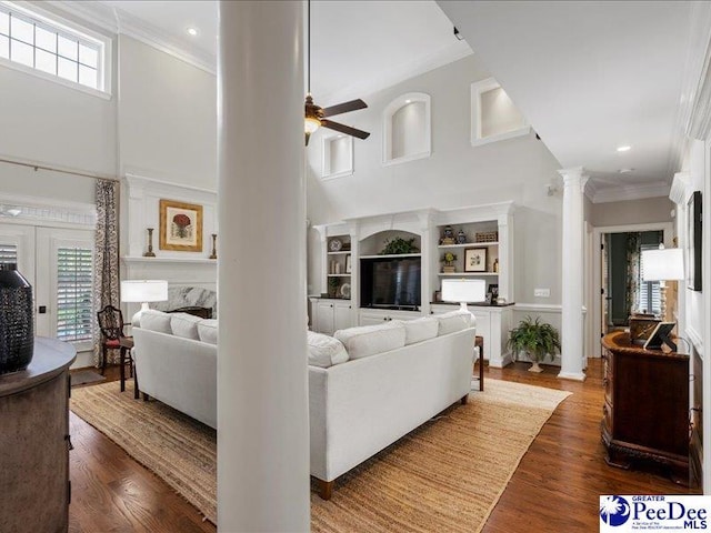 living area featuring crown molding, decorative columns, a towering ceiling, a ceiling fan, and wood finished floors