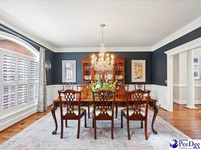 dining area featuring a wainscoted wall, ornamental molding, wood finished floors, and an inviting chandelier