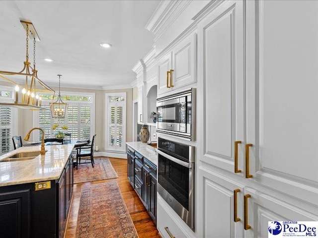 kitchen featuring white cabinets, appliances with stainless steel finishes, ornamental molding, dark cabinets, and a sink