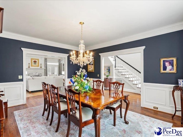 dining room featuring a wainscoted wall, crown molding, a notable chandelier, stairway, and wood finished floors