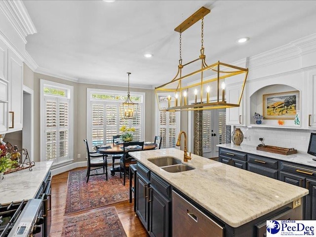 kitchen with stainless steel range with gas cooktop, decorative backsplash, ornamental molding, a kitchen island with sink, and a sink