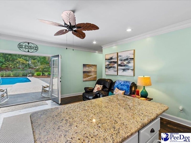 kitchen with light stone counters, crown molding, baseboards, and ceiling fan