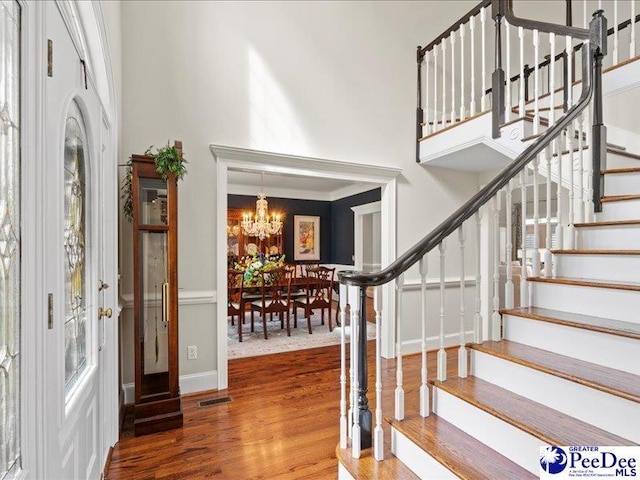 foyer entrance featuring visible vents, a towering ceiling, wood finished floors, stairs, and a notable chandelier