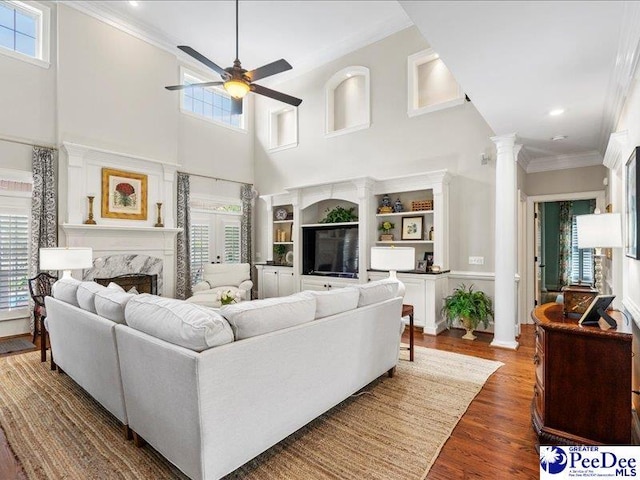 living area featuring a fireplace, wood finished floors, a ceiling fan, decorative columns, and crown molding