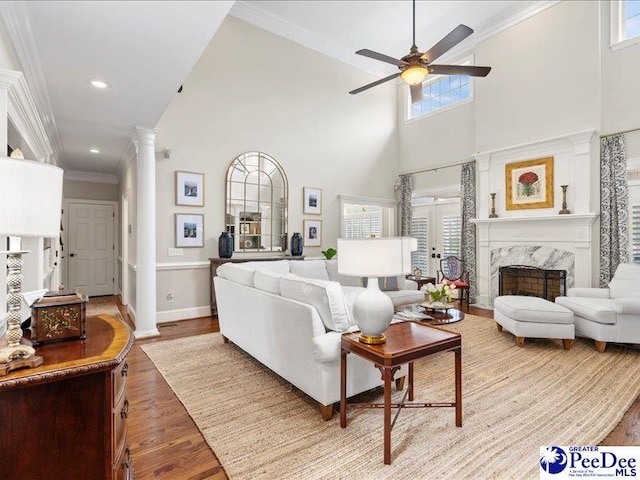 living area with decorative columns, ceiling fan, ornamental molding, light wood-type flooring, and a high end fireplace