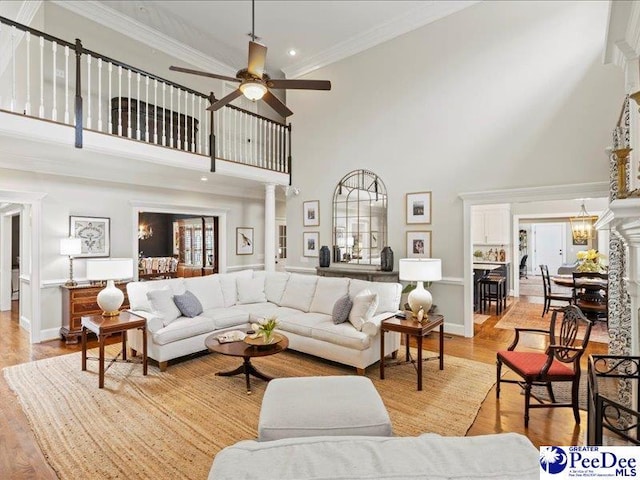 living area featuring ornamental molding, decorative columns, light wood-style flooring, and ceiling fan with notable chandelier